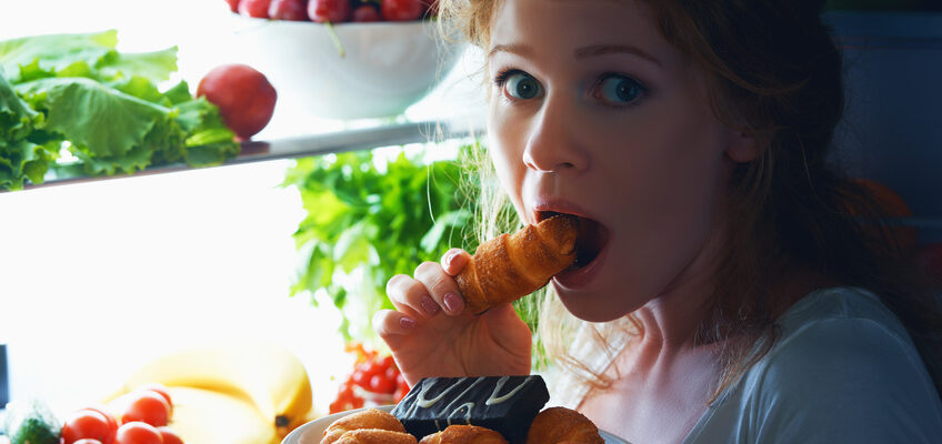 woman eats sweets at night to sneak in a refrigerator